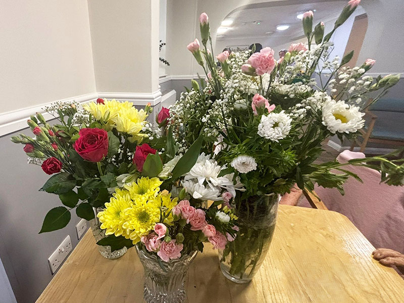 Beautiful floral arrangements in glass vases, featuring roses, chrysanthemums, carnations, and gypsophila on a table at Sonya Lodge Residential Care Home.